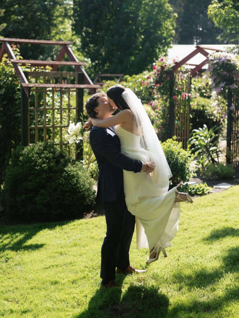 Groom lifting and kissing the bride on the lawn at Froggsong Gardens.