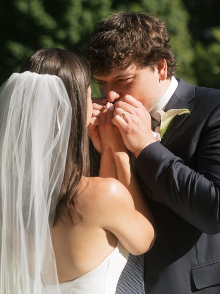 Groom kissing the bride’s hands during newlywed portraits in the gardens.