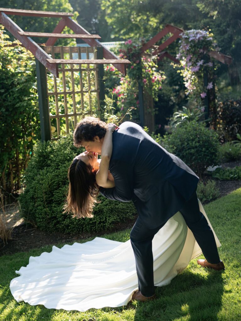 Groom dip kissing the bride during their golden hour Froggsong Gardens wedding portraits.