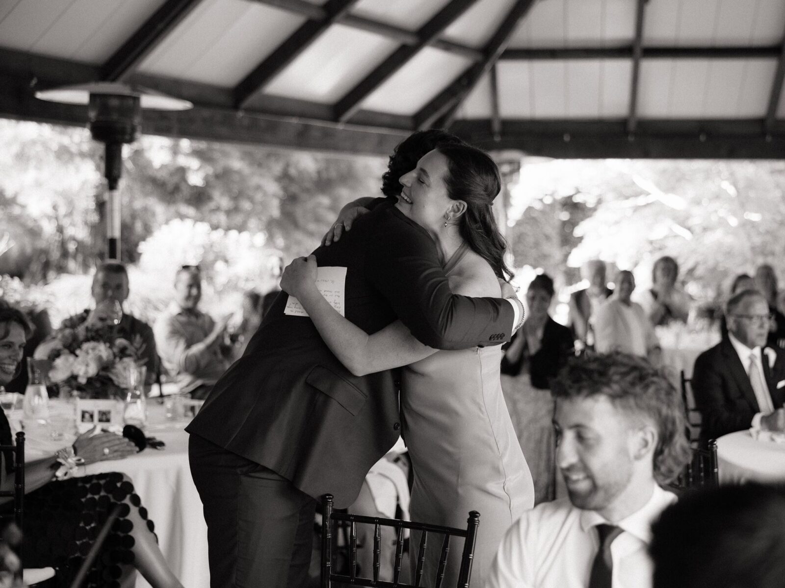 Black and white photo of the groom hugging a bridesmaid.