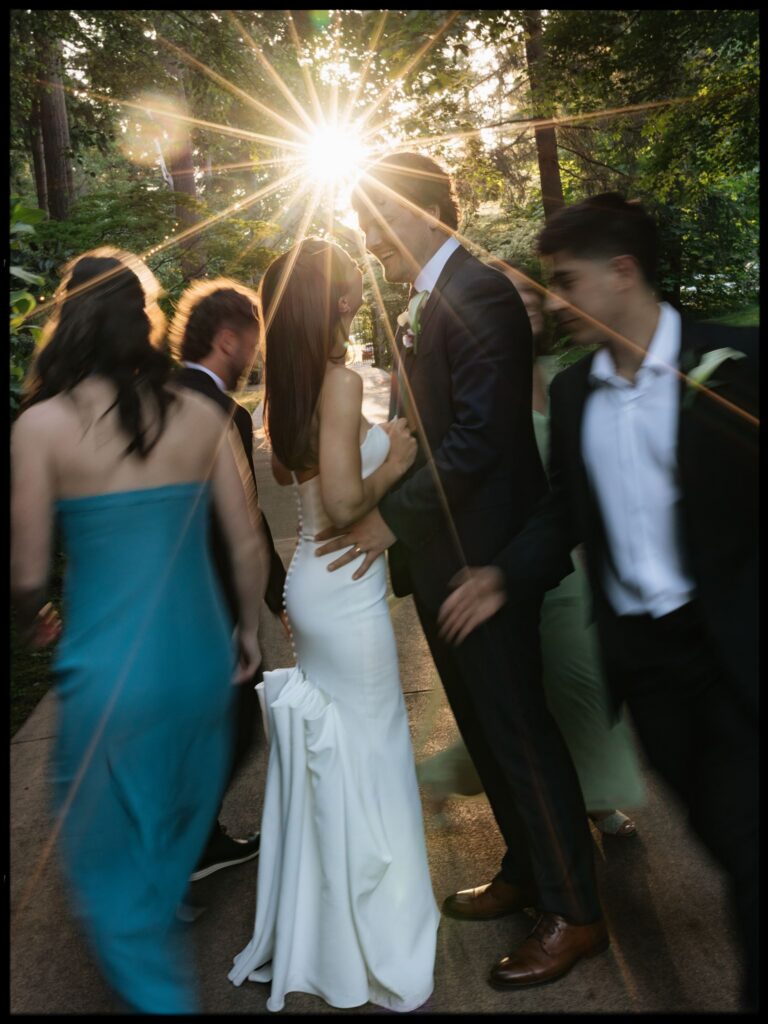 Bride and groom smiling during golden hour wedding party portraits as their wedding party moves around them.
