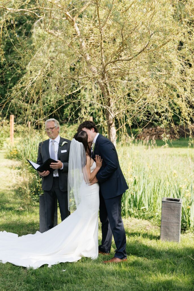 Bride and groom sharing their first kiss beneath a willow tree.