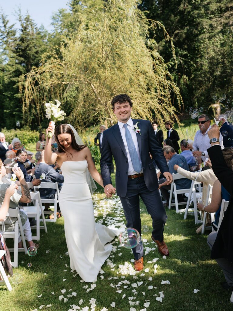Newlyweds walking down the aisle as guests blow bubbles around them.