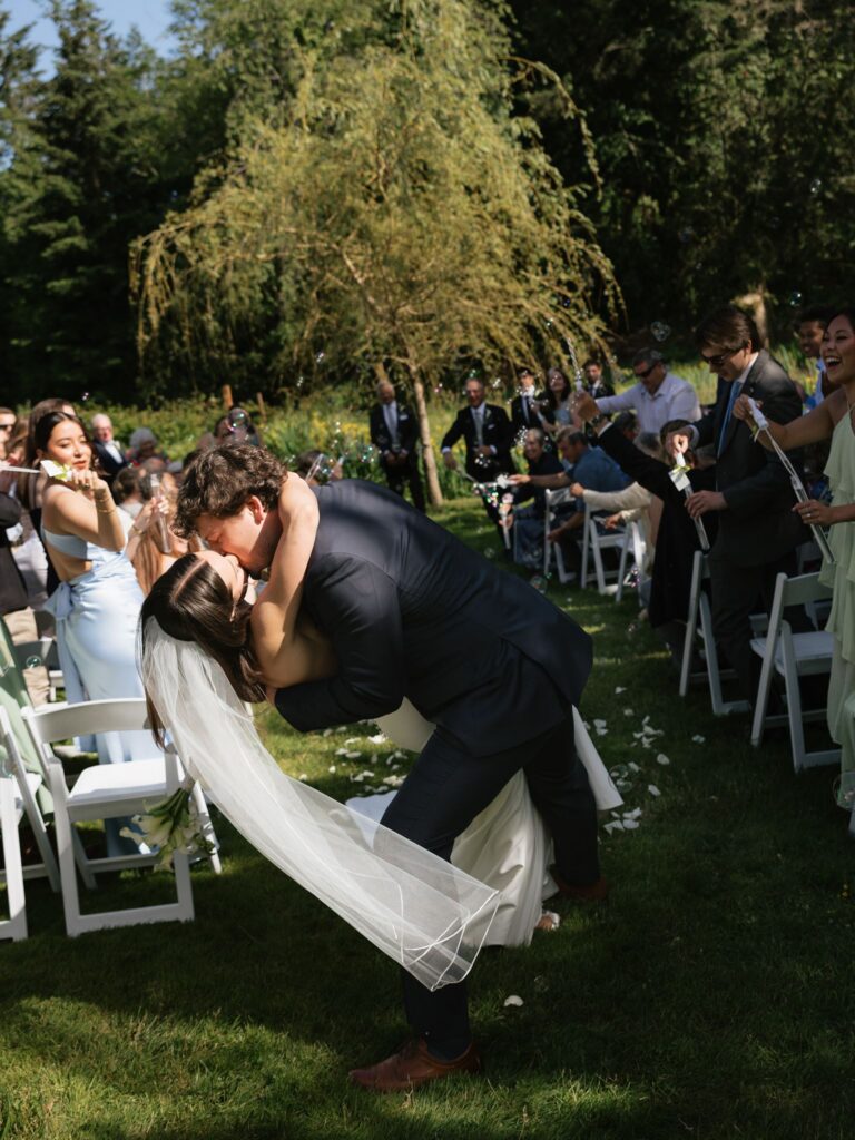 Groom dipping and kissing the bride during their bubble-filled ceremony exit.