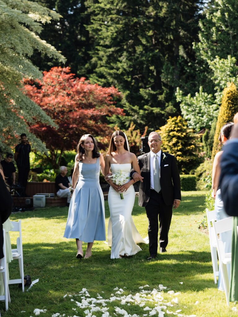 Bride walking down a petal-lined aisle with her parents at Froggsong Gardens.