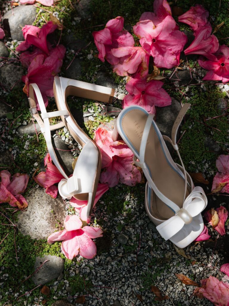 White bow wedding heels arranged among fallen pink flower petals.