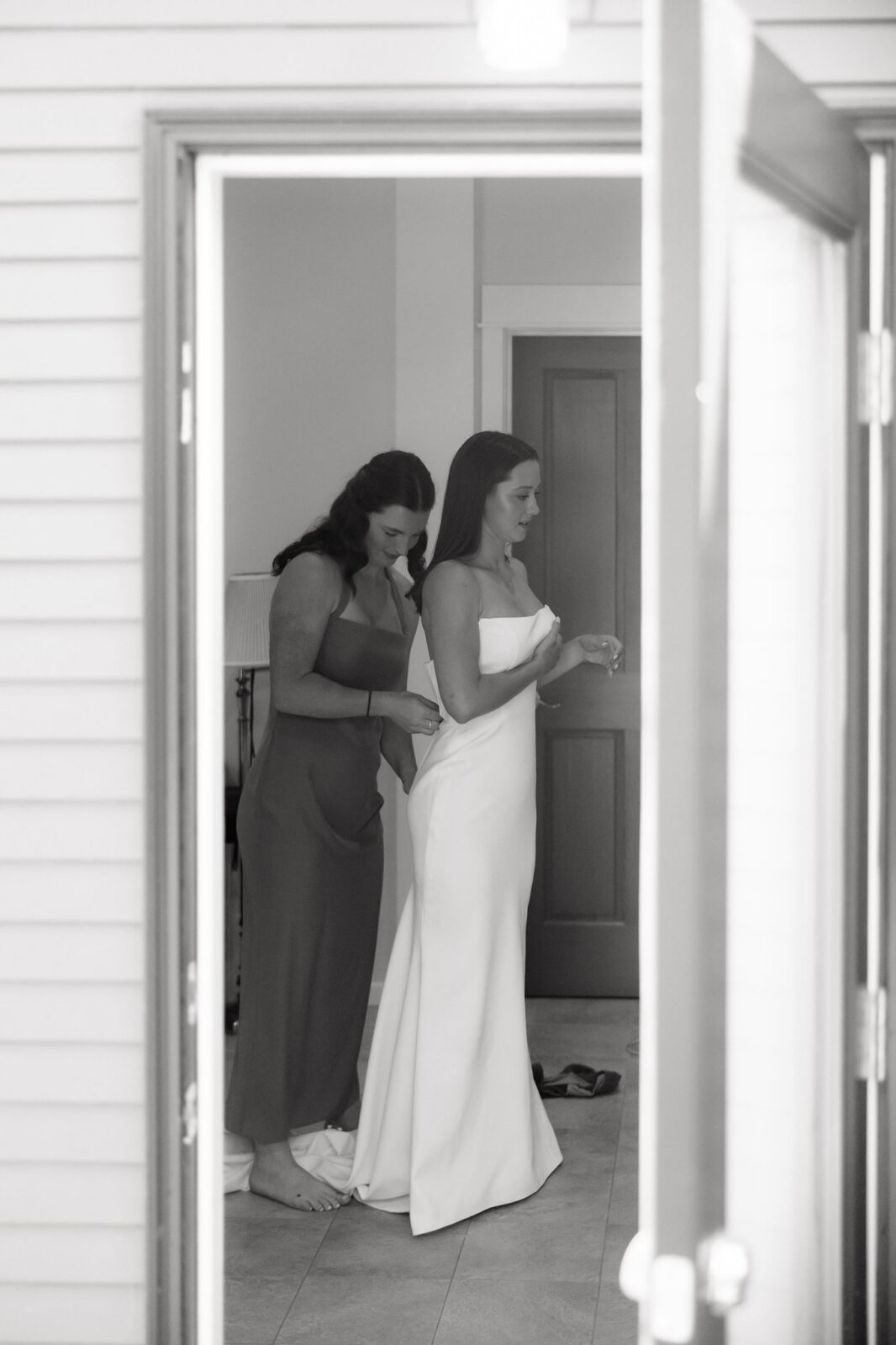 Bridesmaid helping the bride into her strapless wedding dress.