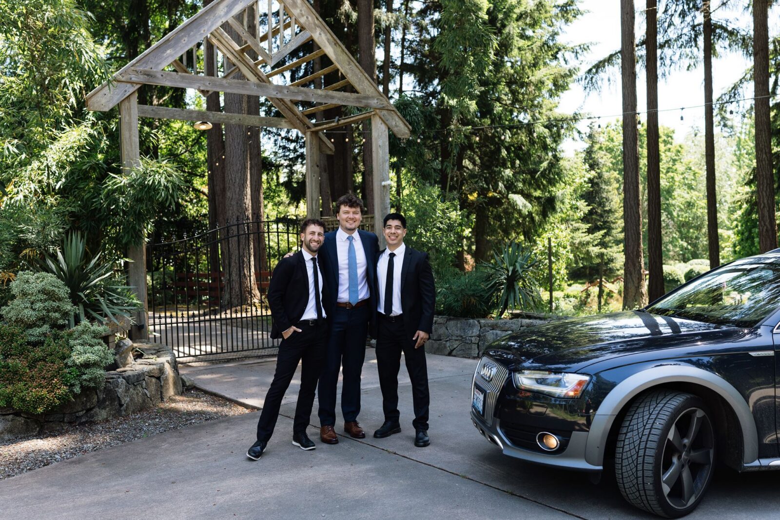 Groom and groomsmen beside a black Audi wagon outside Froggsong Gardens.