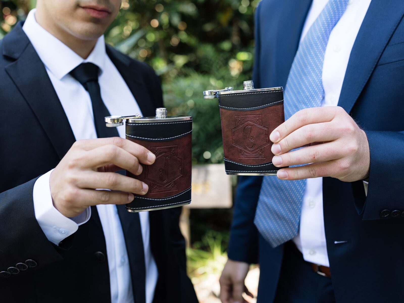 Groom and groomsman holding personalized leather flasks.