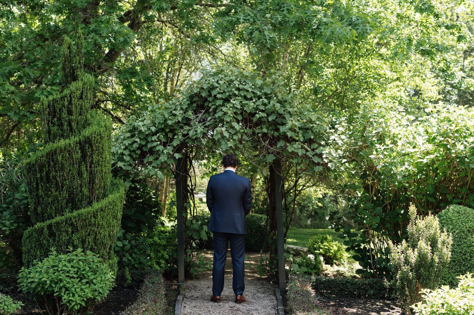 Groom waiting beneath a leafy archway for a first look at Froggsong Gardens.