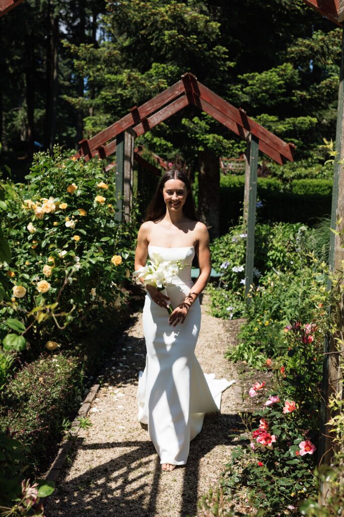 Bride walking through a flower-lined garden path before the first look.