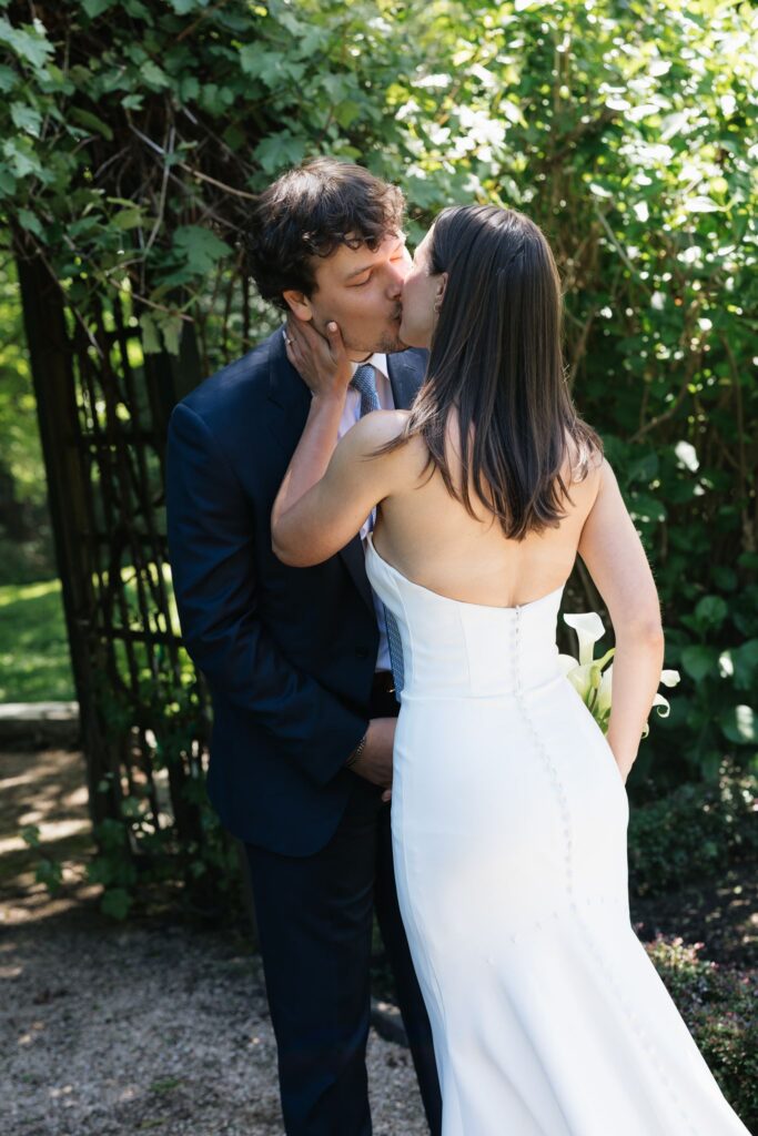 Bride and groom kissing beneath a leafy garden archway.