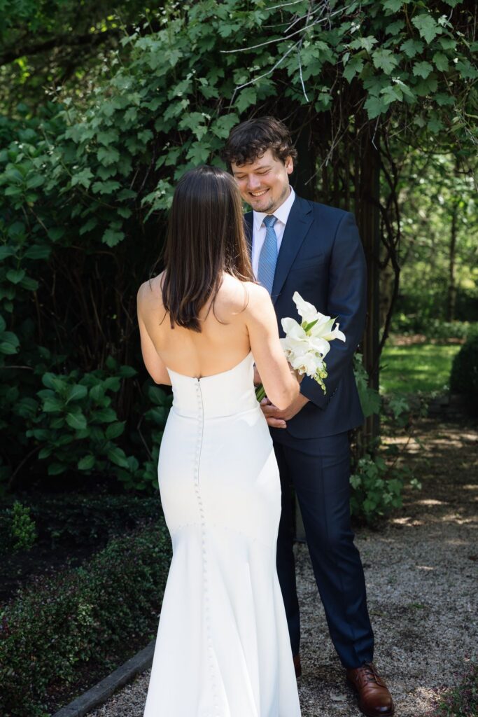 Bride and groom holding hands beneath the greenery at Froggsong Gardens.