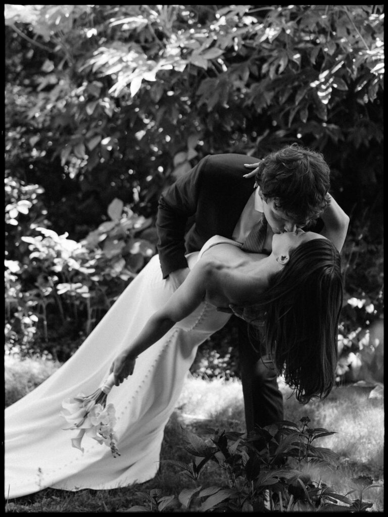 Black and white photo of the groom dipping the bride for a kiss during their Froggsong Gardens wedding portraits.