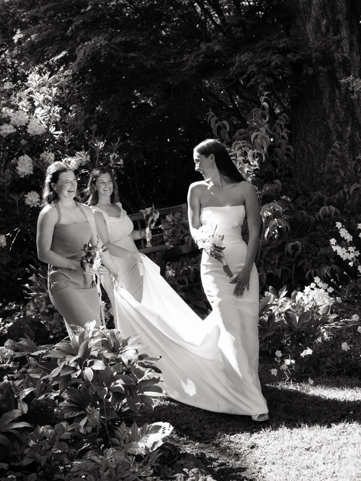 Black and white candid photo of bridesmaids holding the brides train as she walks in front of them.