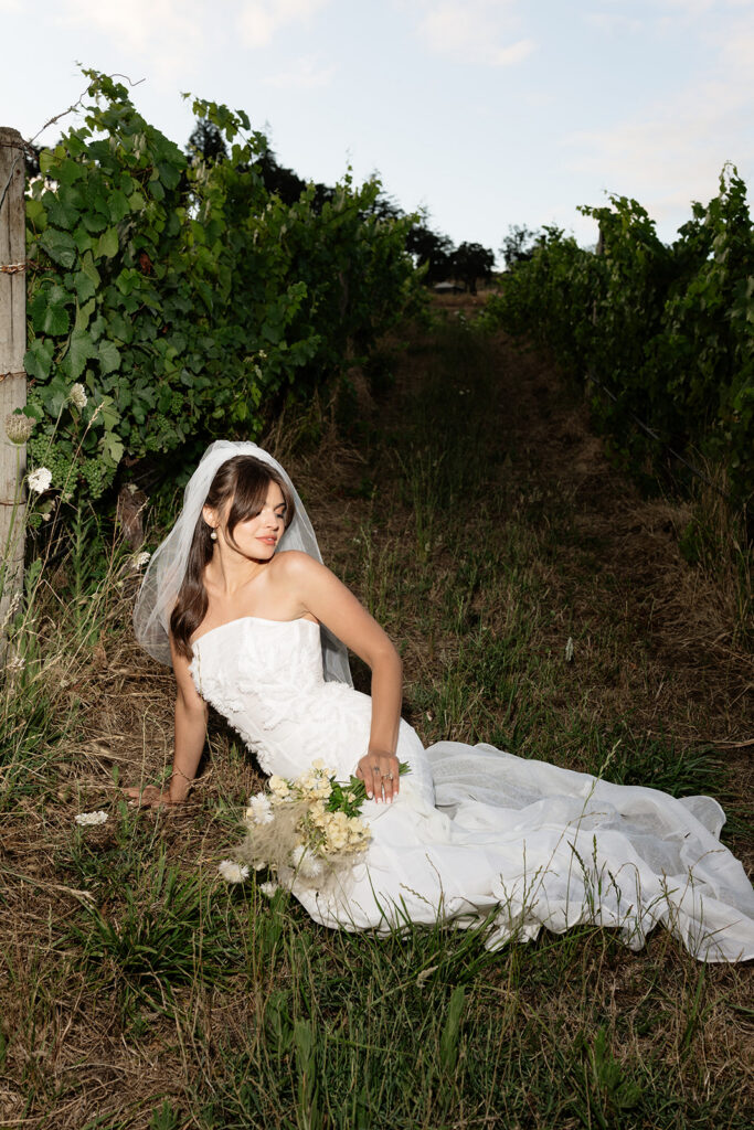 Bride sitting in the grass near the vineyards at Maysara Winery in Oregon.