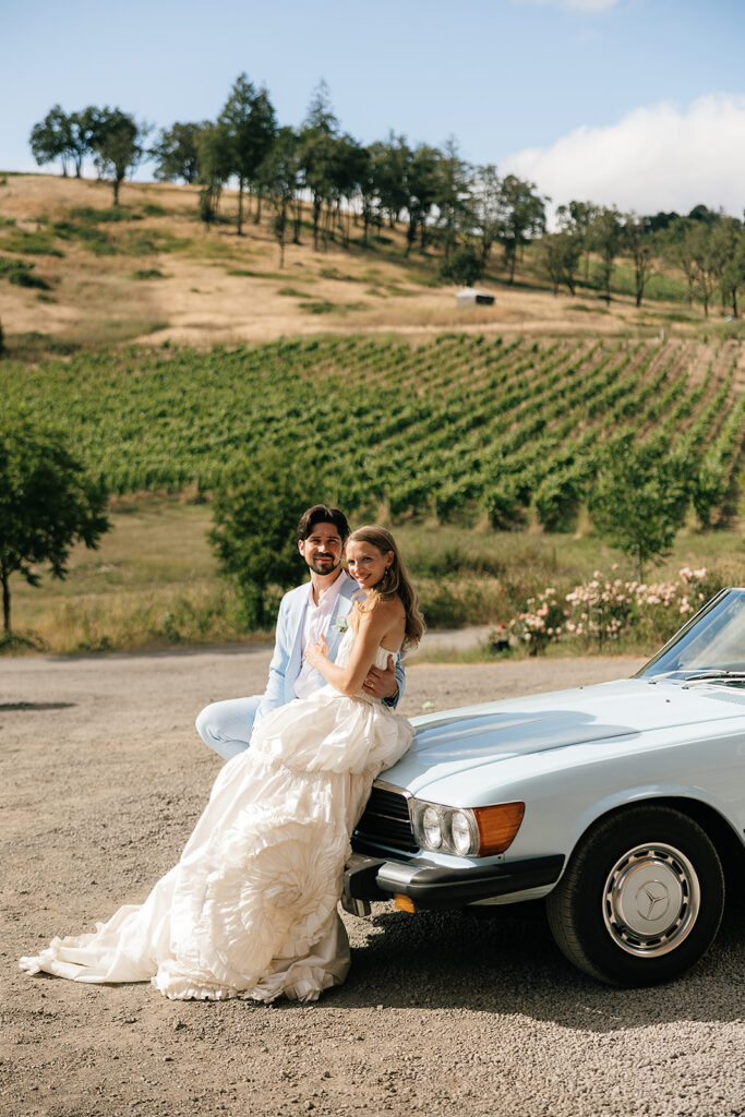 Bride and groom leaning against a vintage blue convertible outside of Maysara Winery for their wedding photos.