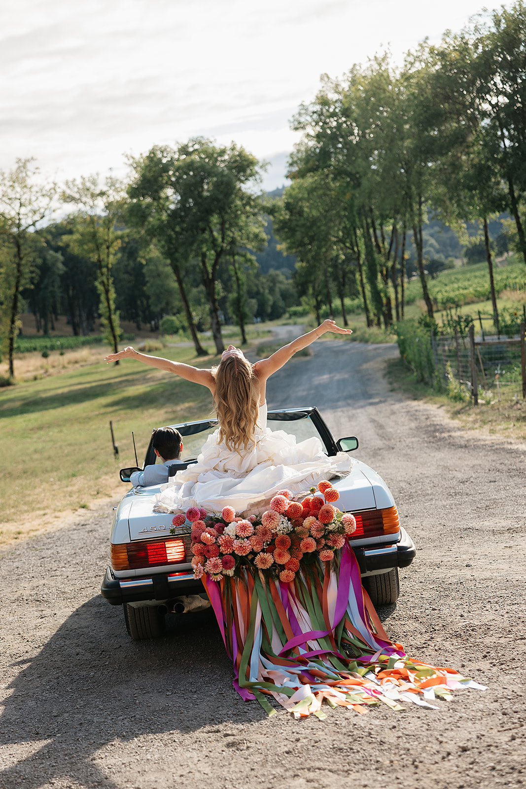 Bride and groom riding down a dirt road in a classic car for their Maysara Winery wedding photos.