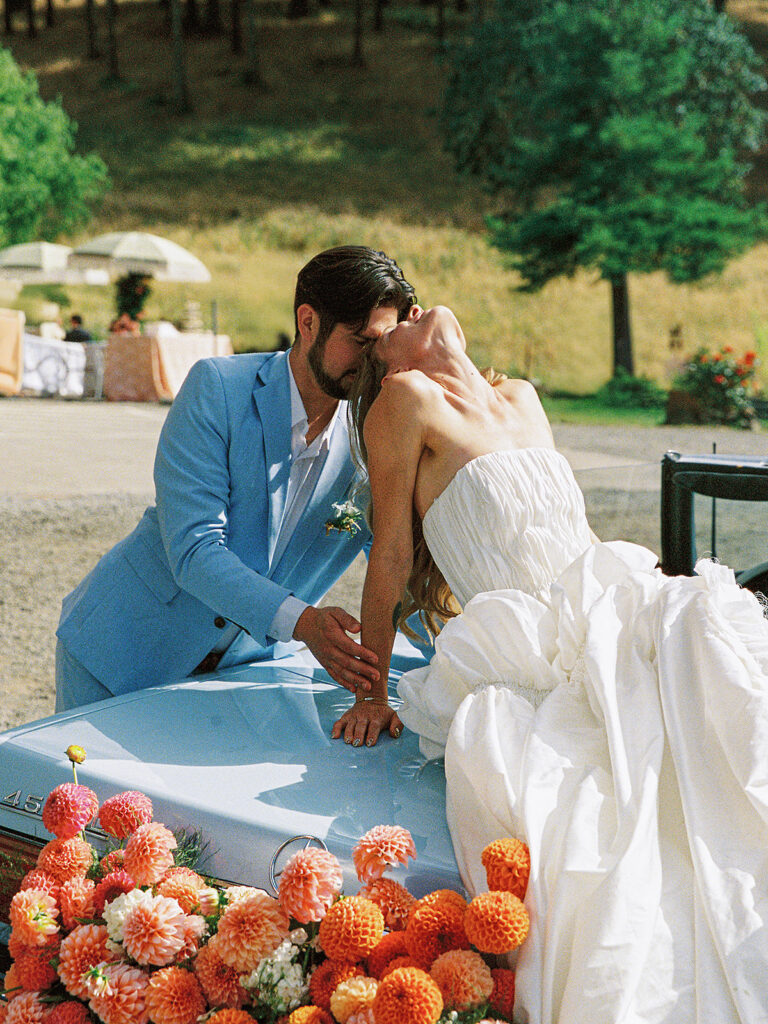 Couple posing on a vintage Mercedes convertible with orange and pink flowers at Maysara Winery.