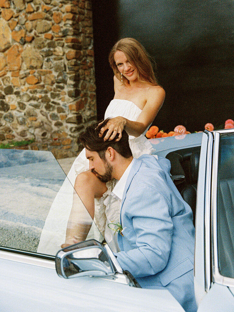 Couple posing together in a vintage convertible beside the stone exterior of Maysara Winery.