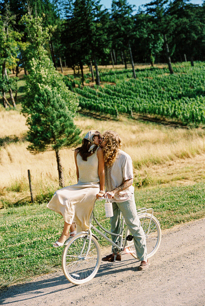 Couple kissing beside a bicycle on a vineyard road at Maysara Winery.