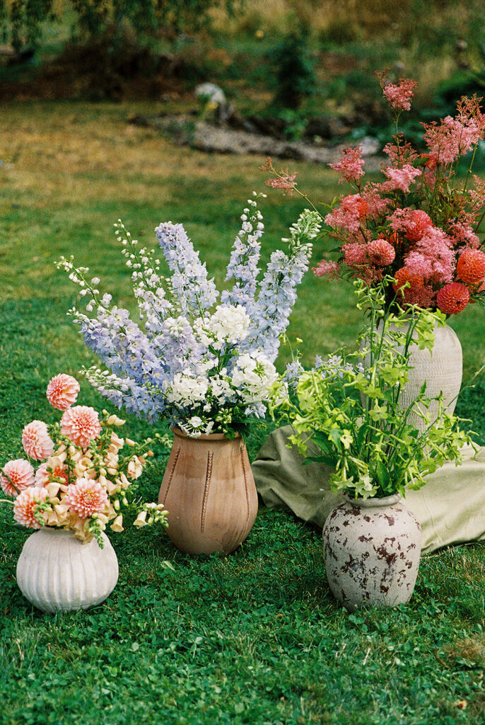 Colorful garden-style wedding florals in ceramic vessels with pink, orange, blue, and white flowers captured on film.