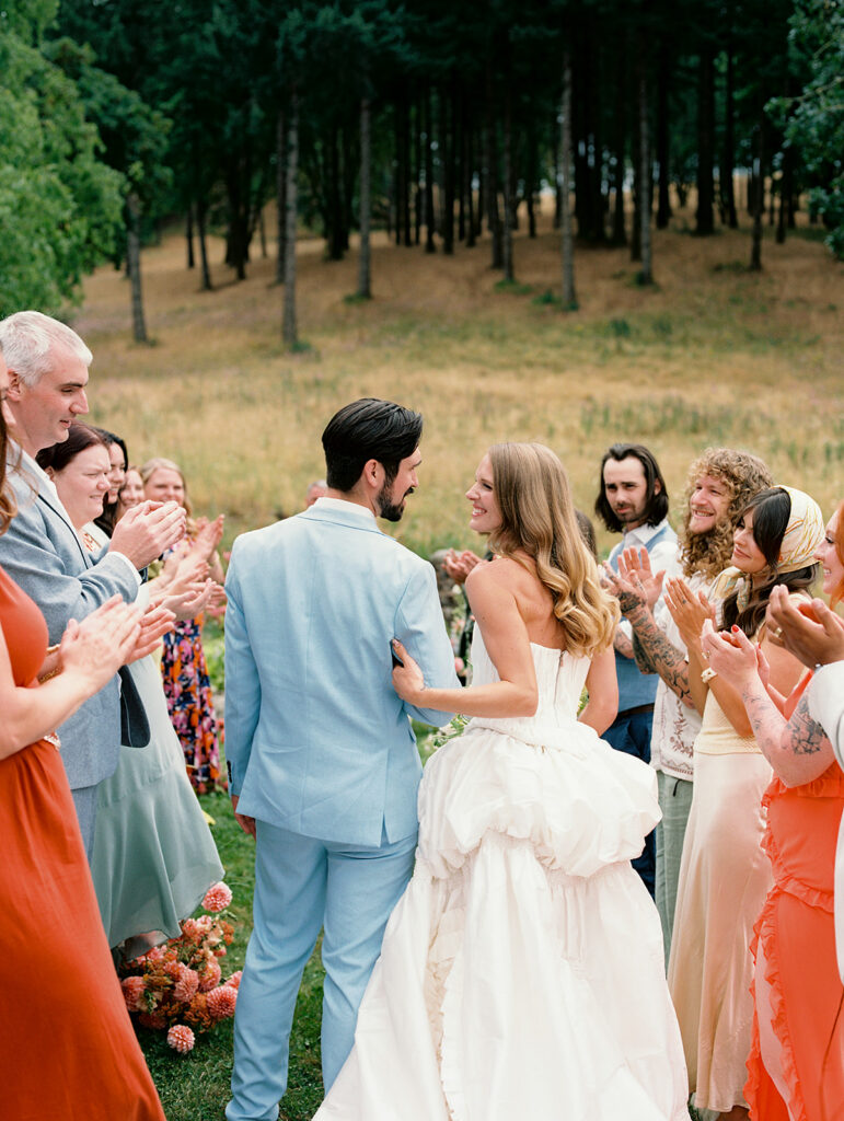 Couple walking back down the aisle after an outdoor ceremony at Maysara Winery as guests clap on both sides captured on film.