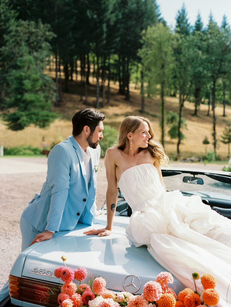 Couple posing on a vintage Mercedes convertible with orange and pink flowers at Maysara Winery.