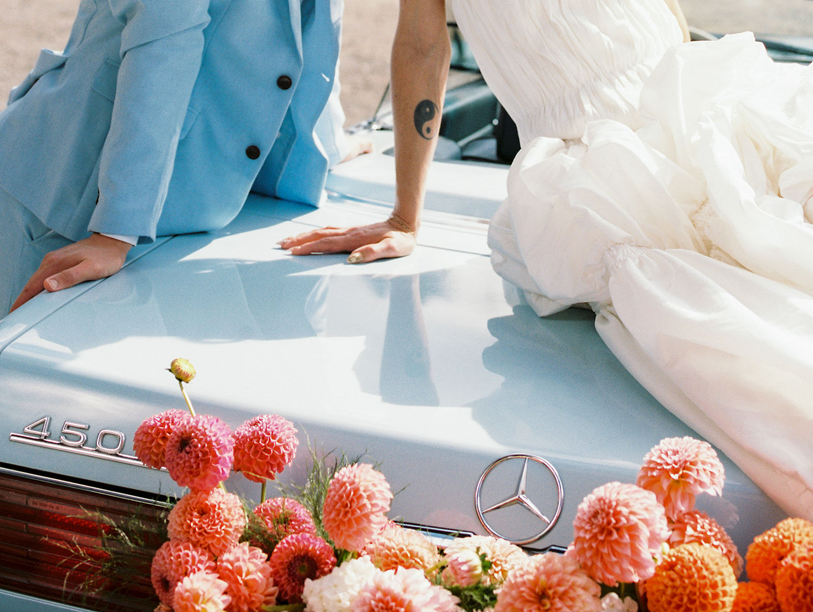 Close up shot of a couple posing on a vintage Mercedes convertible with orange and pink flowers at Maysara Winery.