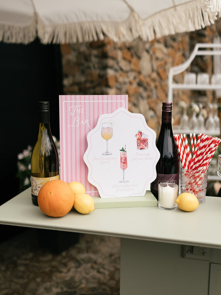 Outdoor cocktail bar at Maysara Winery with wine bottles, citrus, striped straws, and illustrated drink signage.