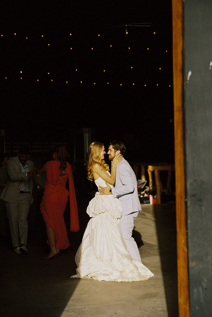Couple dancing during a wedding reception inside Maysara Winery with guests dancing behind them, with the bride in a white gown and groom in a light blue suit.