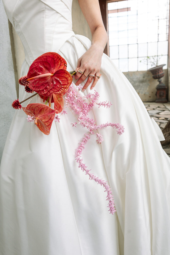 Close-up of red and pink bridal florals against a white wedding gown.