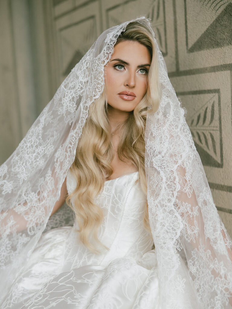 Blonde bride framed by a lace veil in a white bridal gown.
