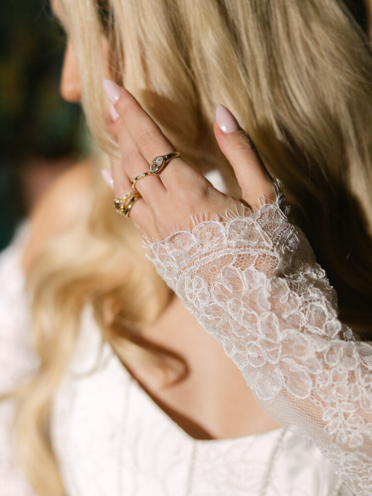 Close-up of lace bridal gloves and stacked gold rings.