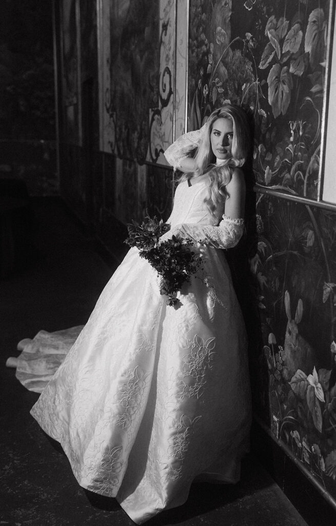 Black and white photo of a bride leaning against a mural inside The Ruins wedding venue in Seattle, Washington.