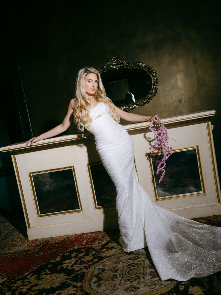Bride posing near a white desk with a pink bouquet.